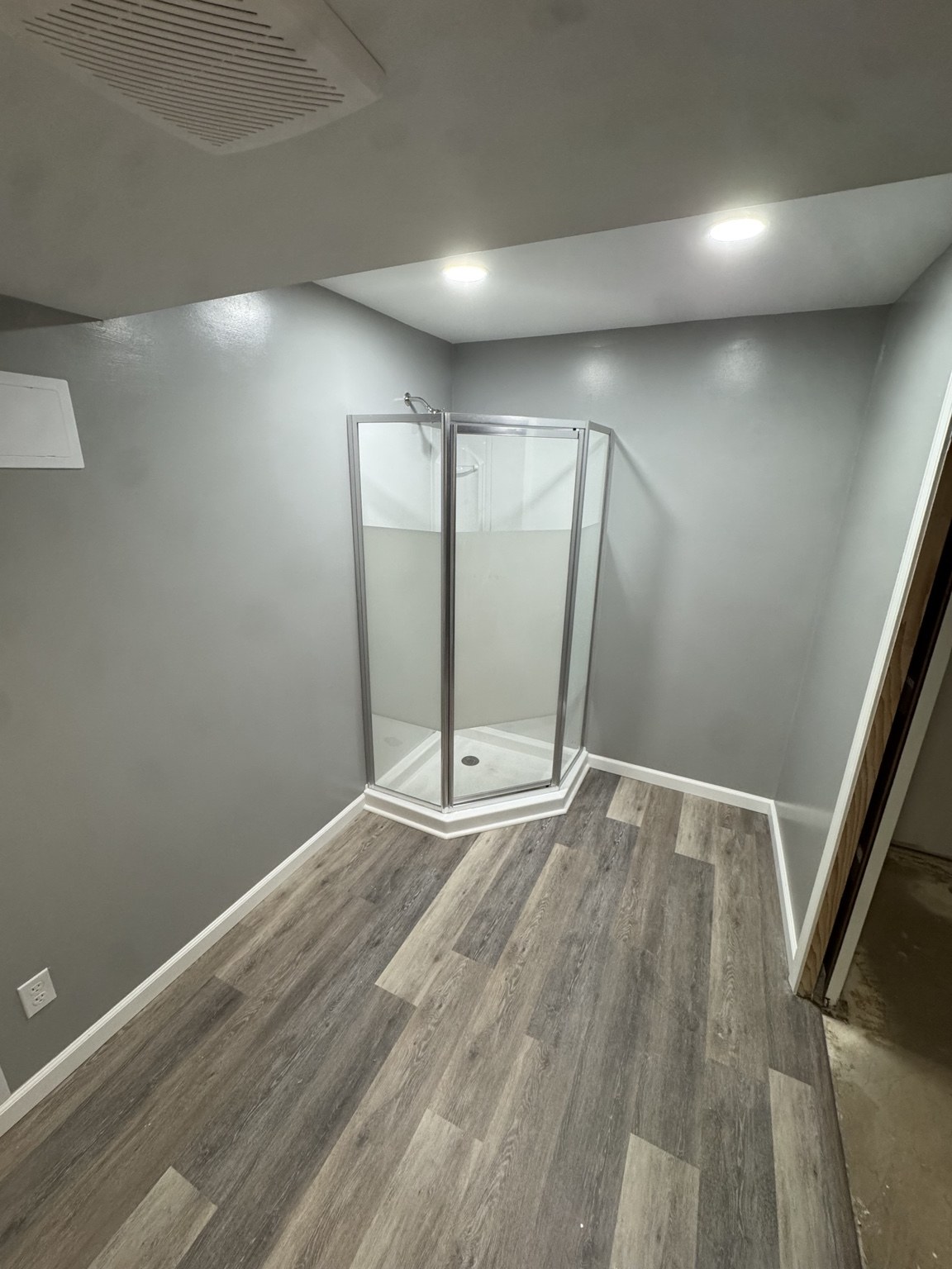 Renovated shower area with glass corner enclosure, gray painted walls, and new wood-look flooring