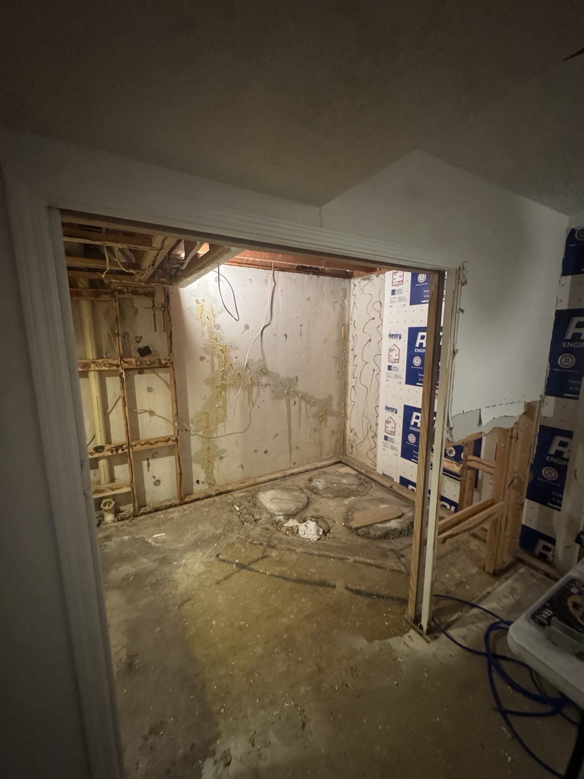 Bathroom shower area before renovation, with stripped walls and exposed floor