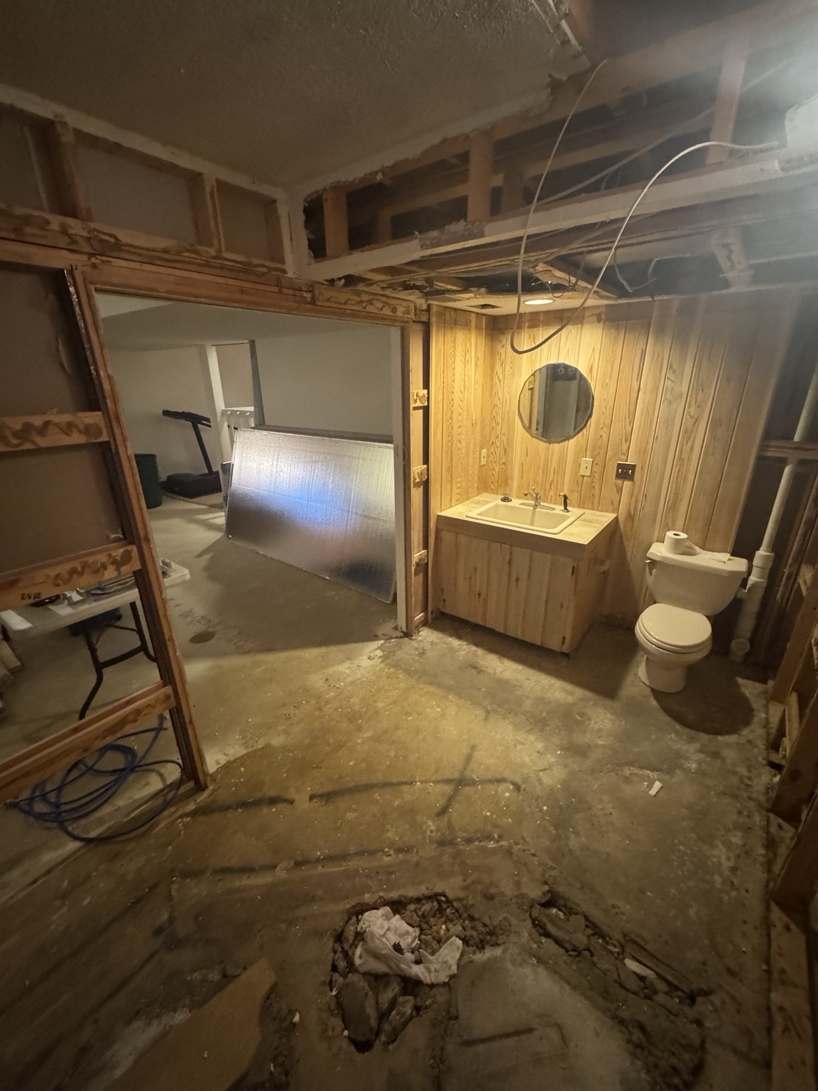 Bathroom before renovation, with exposed framing, bare floor, and an older wood vanity